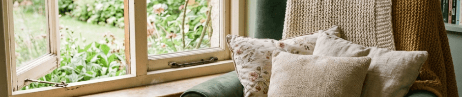 Open book on green armchair beside candle, tea, and garden window